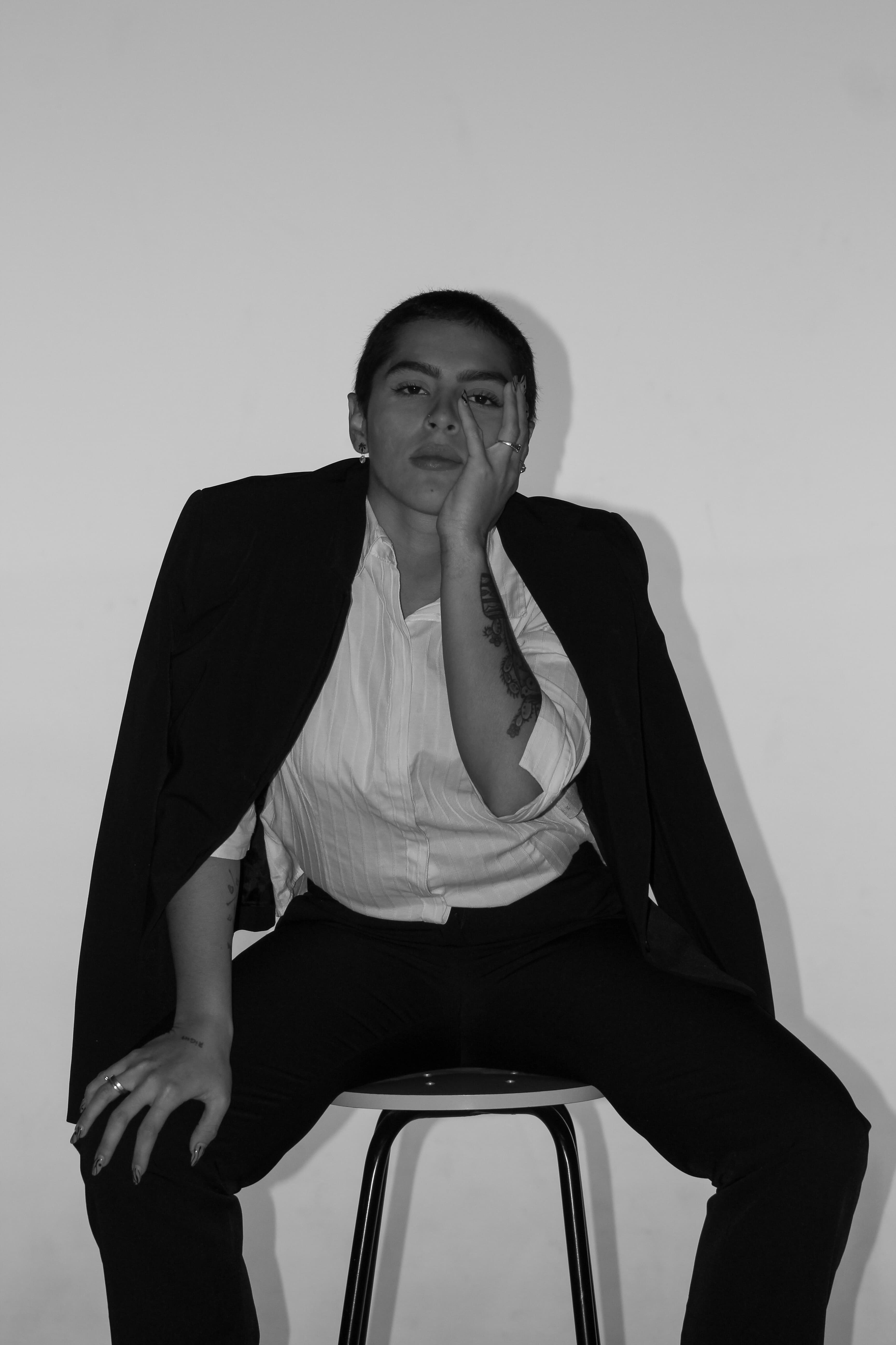 Retrato P&B, sentada de frente com uma mão no rosto, com o blazer apenas por cima.