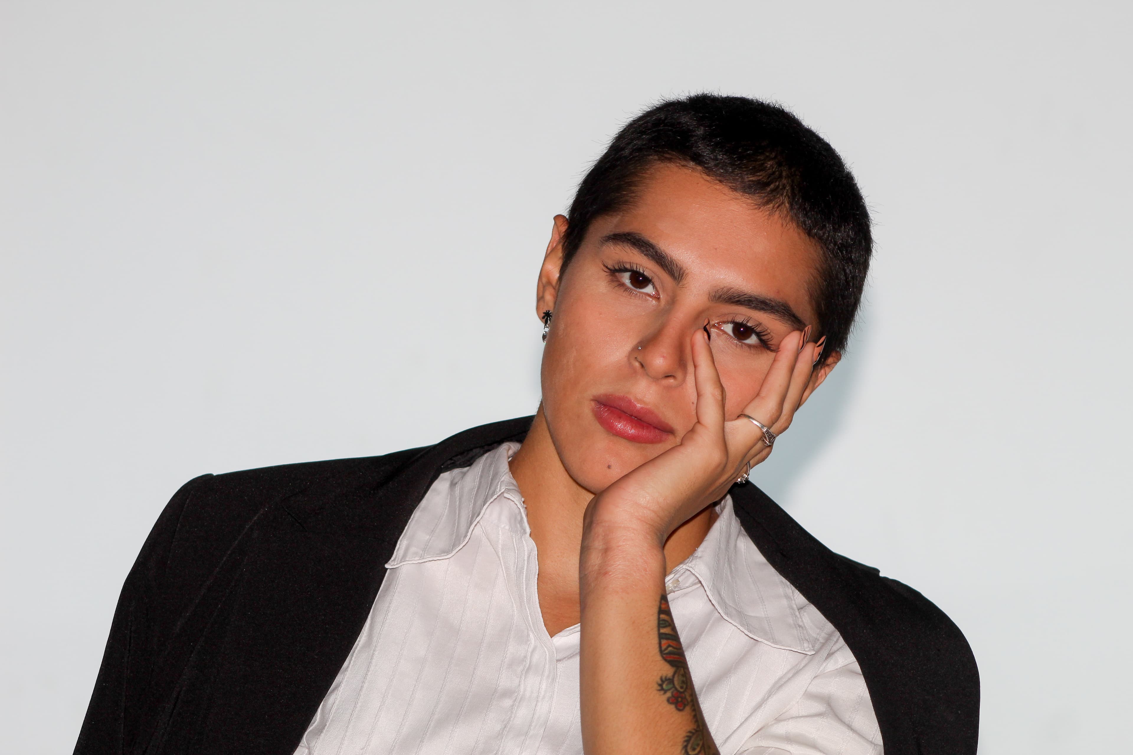 Um pouco caída para o lado com a mão no rosto. Blazer e camiseta social.