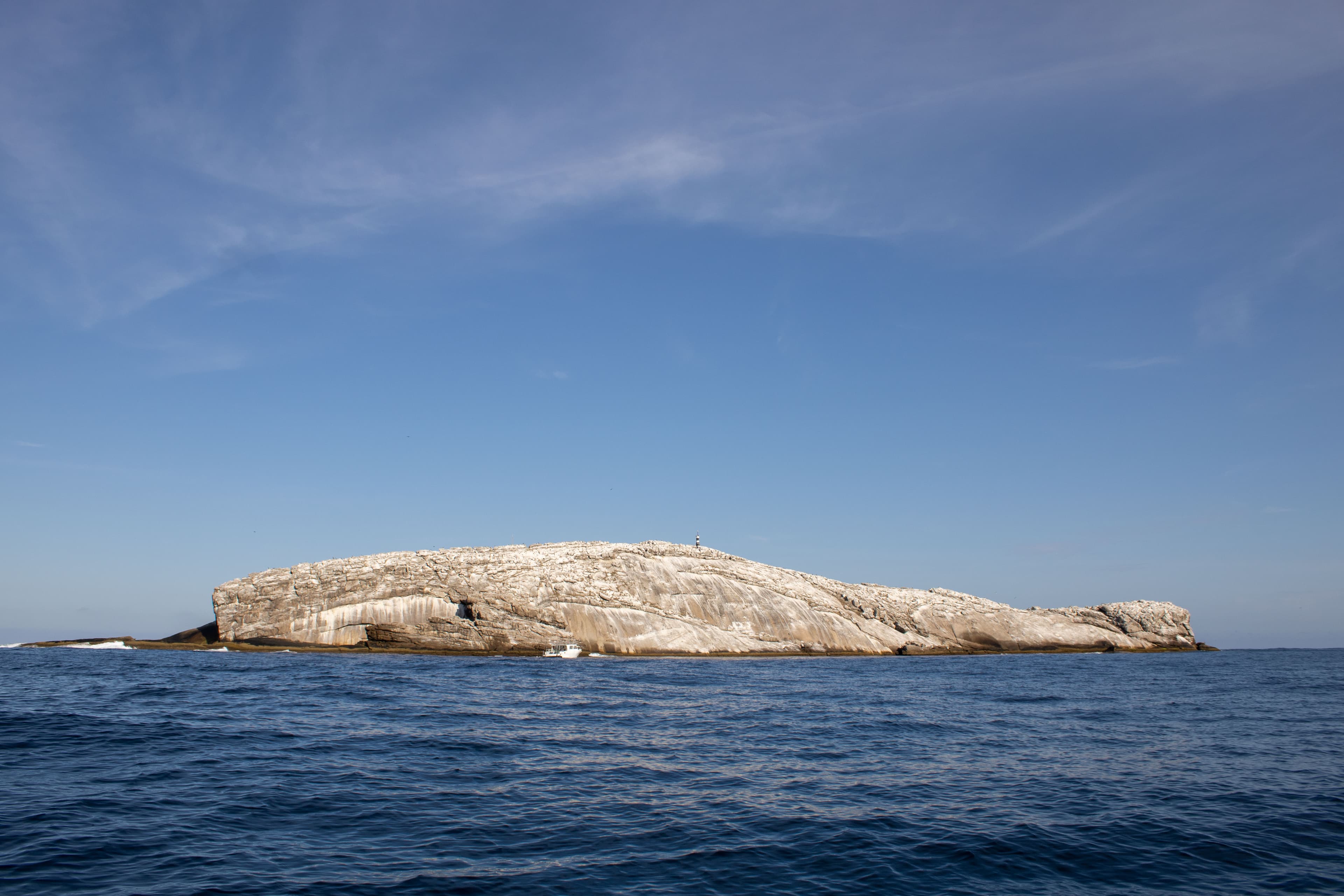 Laje de Santos por completa, sem a presença dos Calhaus. Mar azulado calmo, poucas nuvens, céu azul.
